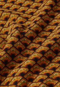 Tissu en tricot présentant un motif de vagues répétées dans des tons chauds d'orange, de vert et de noir, avec une surface texturée et un éclat lisse.