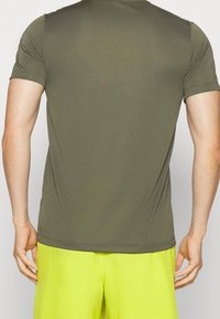 Maglietta atletica verde oliva a maniche corte con una texture liscia, design aderente e cuciture sottili sulle spalle e sull'orlo.