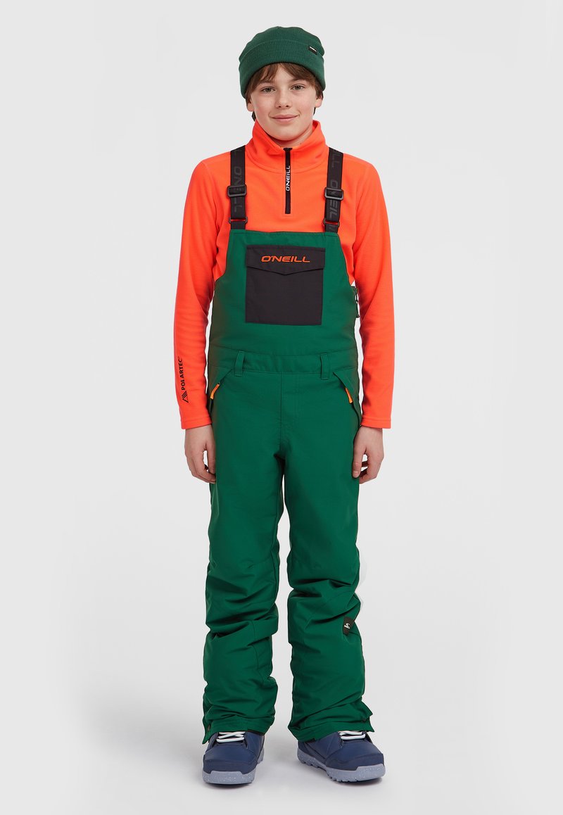 Groene sneeuwoveralls met verstelbare bandjes, een voorzak en oranje accenten, gecombineerd met een feloranje rits-jack en een groene muts.