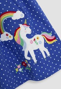Blauw jurkje met stippen, voorzien van een geborduurde witte eenhoorn met een regenboog manen, vergezeld van kleurrijke bloemen en wolkdetails.
