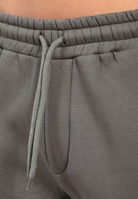 Pantalones deportivos grises con cintura elástica, cordón ajustable y un bolsillo lateral. Textil suave con una textura lisa y uniforme.