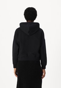 Felpa nera cropped con cappuccio regolabile, polsini e orlo a costine. Presenta una superficie liscia, una vestibilità oversize e una silhouette rilassata.