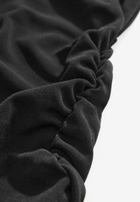 Tissu noir avec un détail élastique froncé créant une texture plissée sur une surface textile lisse.