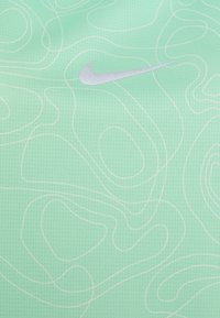 Nike-stof in lichtgroen met een gestructureerd oppervlak, voorzien van een wit contourpatroon en een zilveren Nike-logo aan de rechterkant.