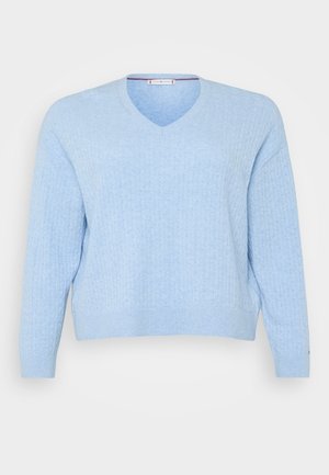 Lys blå genser med ribbestruktur, V-hals design og lange ermer med avslappet passform. Klassisk strikkemønster gjennom hele.