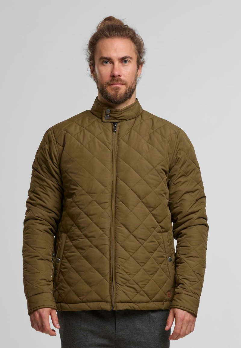 Vihreä tikattu takki, jossa on pystykaulus, vetoketju ja napit. Takissa on sivutaskut ja teksturoidut ompelukuvio.