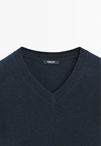 Marineblauwe v-hals trui met een geribbelde kraag en manchetten, gemaakt van zacht breimateriaal, met een klein zwart label binnenin.