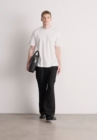 Biele bavlnené tričko, čierne nohavice, nesie čiernu koženú tašku. Jednoduchý dizajn, rovný strih, s hladkou textúrou a bez vzorov.