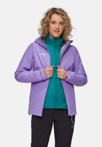 Chaqueta impermeable morada con capucha sobre una capa de cremallera azul verdosa. La tela parece suave, con cremalleras y un logo en la parte delantera.