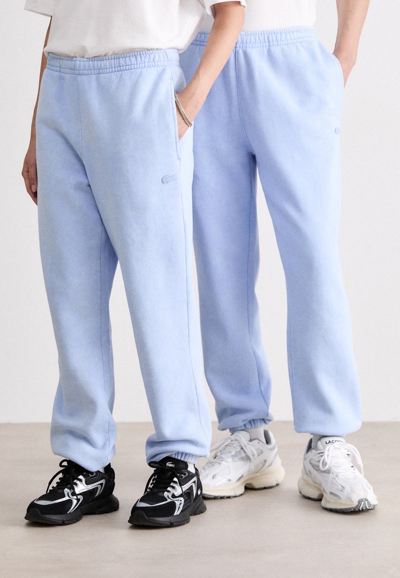 Pantalones de chándal azul claros con cinturilla elástica y bolsillos laterales. Tejido suave con una textura sutil. Presenta un pequeño logo bordado.