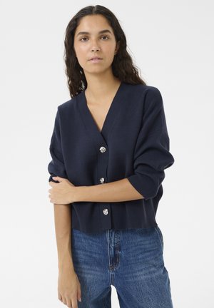 Navy blue knitted cardigan with a deep V-neck and three oversized silver buttons. Features loose, slightly cropped sleeves and a soft texture.