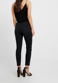 Svart ärmlös topp med vertikal ribbad textur, kombinerad med högmidjade svarta skinny jeans och klacksandaler med blockklack.