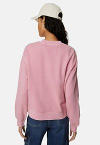 Sudadera rosa de corte relajado, con puños y dobladillo acanalados. Complementada con una gorra de color claro. Textura suave y detalles mínimos.