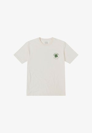 Camiseta de algodón crema con mangas cortas, cuello redondo y un logo de trébol verde con texto en el lado izquierdo del pecho.