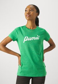 Zielona bawełniana koszulka z białym logo "Puma" i małym akcentem logo. Koszulka ma okrągły dekolt i krótkie rękawy.