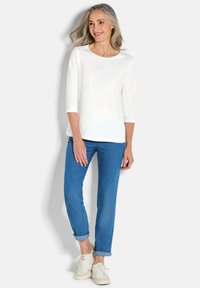 Witte driekwart mouwtop gecombineerd met opgerolde blauwe jeans en witte sneakers. Glad materiaal met een ontspannen pasvorm en ronde halslijn.
