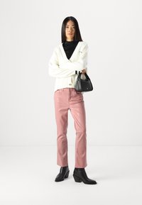 Cardigan in maglia avorio con scollo a V, jeans in denim rosa e stivali neri con tacco. Piccola borsa nera. Design semplice, texture liscia e forma aderente.