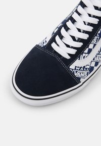 Marinblå mockaskor med vita snören, rutmönster på sidan och en vit gummisula med en svart accentrand.