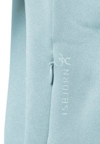 Ljusblå sweatshirt gjord av mjukt material, med dragkedja på sidan och präglad "ISBJÖRN"-logotyp. Texturerad väv och minimalistisk design.