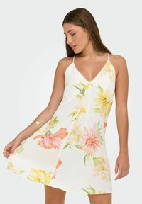 Model in een bloemenjurk zonder mouwen met roze, gele en groene patronen, die gracieuze poses aanneemt terwijl ze de zoom van de jurk vasthoudt.