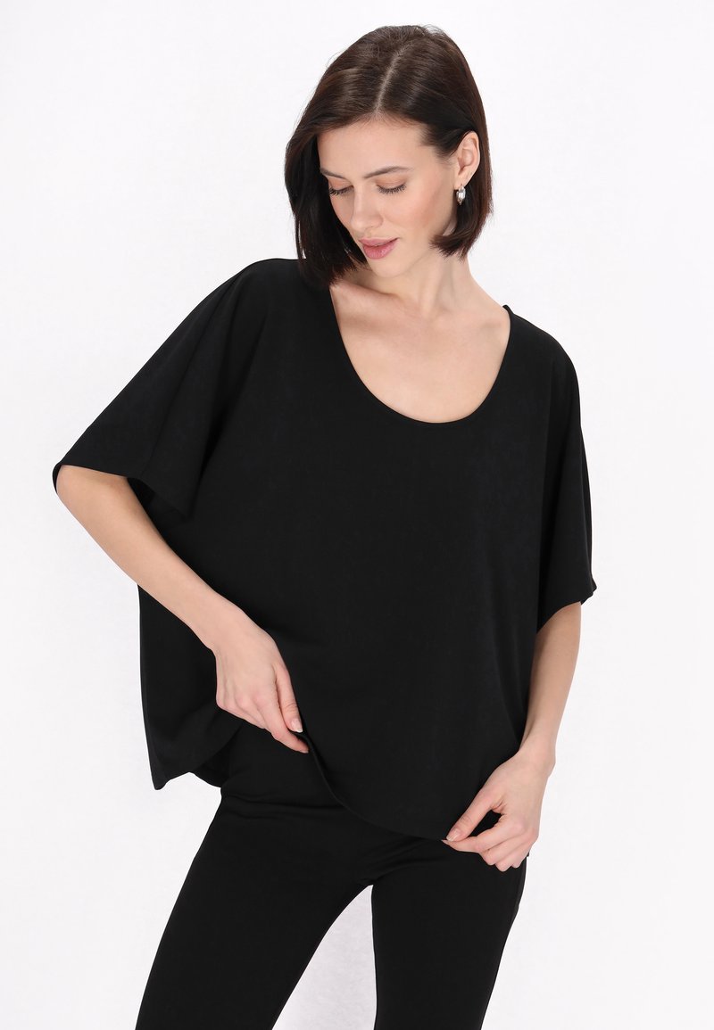 Top supradimensionat negru cu decolteu rotund, mâneci scurte și o textură moale, asortat cu pantaloni negri mulați. Design simplu și versatil.