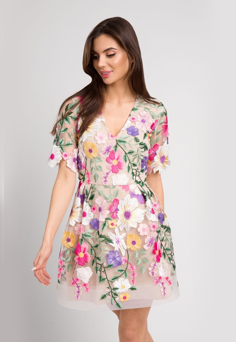 Lekka, prześwitująca sukienka z dekoltem w kształcie litery V, z kolorowym haftem kwiatowym w odcieniach różu, fioletu i żółci na cielistym tle.