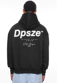 Svart hettegenser med stor hvit tekst "Dpsze™", "SINCE 2020 CREW" og "Elite League 2020" trykket på baksiden. Mykt stoff, vanlig passform.