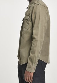 Olivgrön, långärmad skjorta med knäppbara bröstfickor, krage och avslappnad passform. Tillverkad av mjukt, texturerat tyg med en något urtvättad finish.
