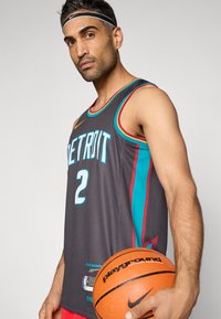 Szürke kosárlabdamez akvamarinkék és bordó díszítéssel; a "DETROIT" felirat és a "2" szám látható rajta. A játékos egy narancssárga kosárlabdát tart.