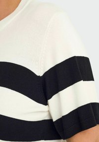 Maglione lavorato a maglia a righe bianche e nere con maniche corte, caratterizzato da un scollo a V e una texture liscia. Le righe variano in larghezza.
