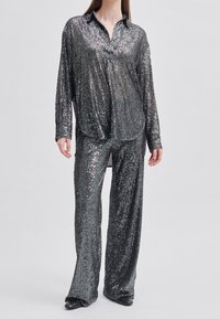 Funkelndes schwarz-silbernes Paillettenkleid mit einem locker sitzenden Hemd mit Kragen und passenden Hosen, mit einer glatten, strukturierten Oberfläche.