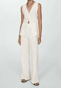 Dzianinowy krótki top z dekoltem w serek i guzikami w kolorze kremowym, zestawiony z szerokimi spodniami o szerokich nogawkach z teksturowanej tkaniny. Noszony z płaskimi sandałami.