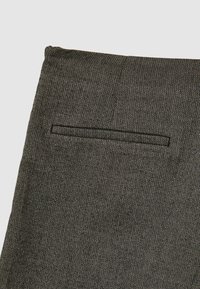 Stoff im Fischgrätmuster in Schwarz und Creme mit einem flachen Taschendetail. Das Material wirkt strukturiert und texturiert, geeignet für maßgeschneiderte Stile.