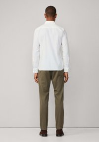 Camisa blanca de manga larga con cuello abotonado, combinada con pantalones en verde oliva. La camisa presenta un diseño sencillo con botones en los puños.