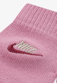Růžová pletená ponožka s žebrovaným vzorem a vícebarevným vyšívaným logem Nike, měkkou texturou a střední výškou.