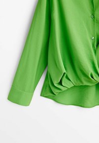 Blouse à manches longues vert vif avec boutons sur le devant et détail drapé noué à la taille sur fond blanc.