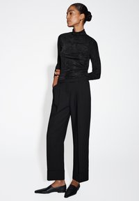 Maglione nero a maniche lunghe con colletto a dolcevita e finitura testurizzata, abbinato a pantaloni neri a vita alta e vestibilità morbida e ballerine nere a punta.