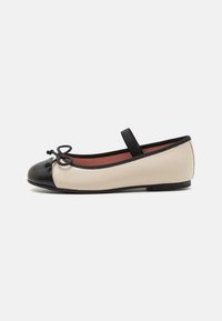 Ballettleilighet med en beige skinnkropp, svart rund tå, og en dekorativ sløyfe med svart stropp. Flat såle for komfortabel bruk.