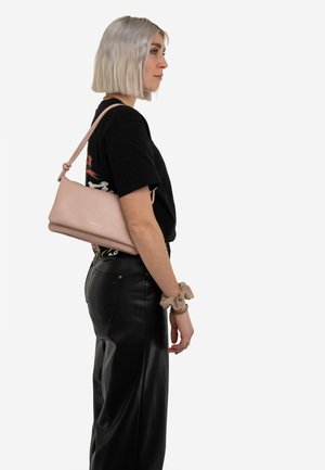 Różowa skórzana torebka o eleganckim, prostokątnym kształcie i węzłowym pasku, noszona na ramieniu w zestawieniu z czarnym outfitem.