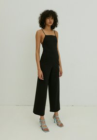 Zwarte jumpsuit met dunne banden en wijde broekspijpen, gemaakt van een soepele stof. Gecombineerd met lichtblauwe, gestrikte hoge hakken. Eenvoudig en modern ontwerp.