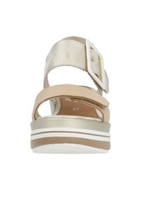 Sandale beige et dorée avec une large bride à l'avant, une bride de cheville ajustable à boucle, et une semelle superposée avec des accents blancs et marron.
