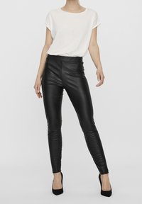 Svarta faux läderleggings med hög midja, i kombination med en löst sittande vit T-shirt. Modellen bär svarta högklackade skor.