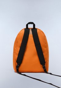 Zaino arancione con una texture liscia, spallacci neri regolabili e una maniglia superiore, caratterizzato da un design arrotondato e senza loghi visibili.