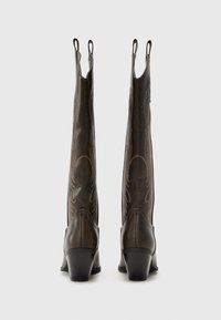 Hnědé kožené kozačky sahající ke kolenům s hladkým povrchem, zdobené dekorativním prošitím a s blokovým podpatkem. Na vrchu je poutko pro snadné obouvání.