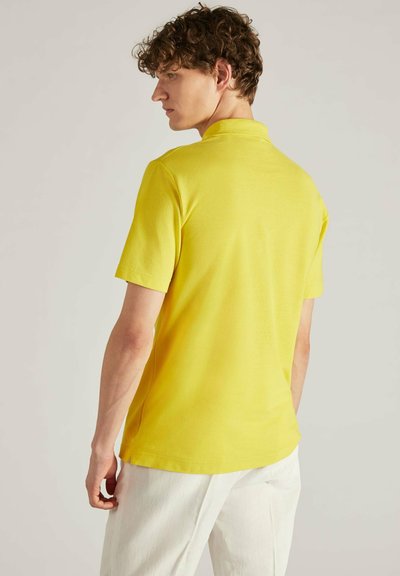 Geel poloshirt met korte mouwen, gemaakt van katoen, met een klassieke kraag en een gladde textuur, gedragen met witte broek.