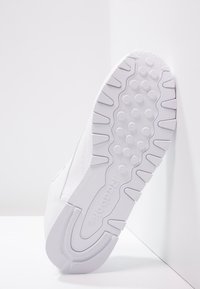 Vit Reebok-sneaker sula med strukturerade greppmönster och Reebok-logotyp, vinklad mot en vit bakgrund med hörn.