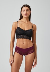 Zwarte kanten bralette met dunne bandjes en een geplooid middengedeelte, gecombineerd met bordeauxrode shorts met kanten afwerking en golvende randen.