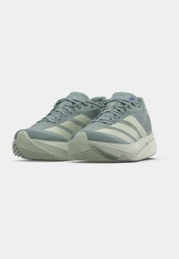 Ζευγάρι γκρίζα και εκρού αθλητικά παπούτσια Adidas με κορδόνια και ρίγες Adidas σε λευκό φόντο.