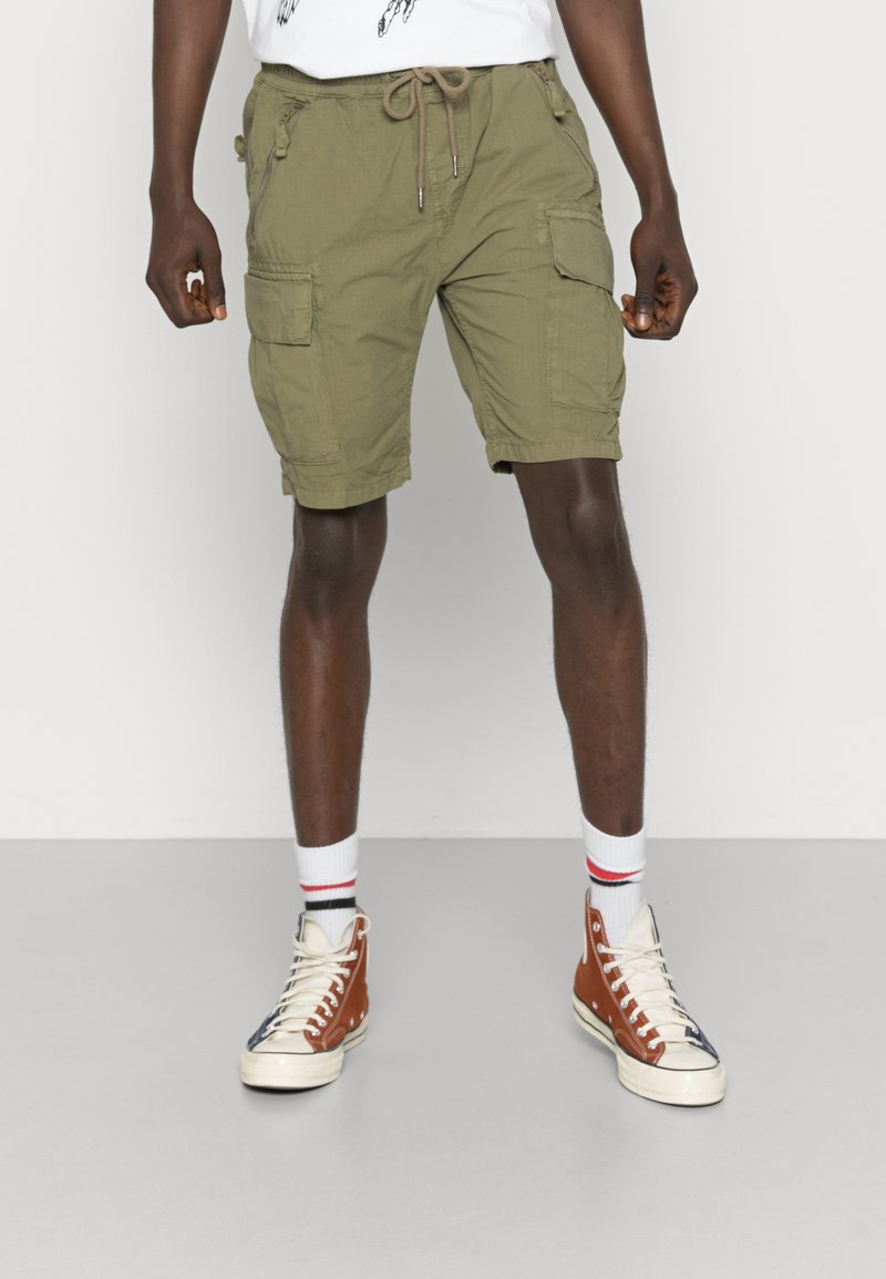 Olijf groene cargoshorts met meerdere zakken, een trekkoord in de taille en een relaxte pasvorm. Draag ze met witte en bruine hoge sneakers.