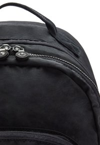 Mochila negra con un exterior suave, cierres de doble cremallera, un asa en la parte superior y sutiles detalles de costura a lo largo de los bordes.